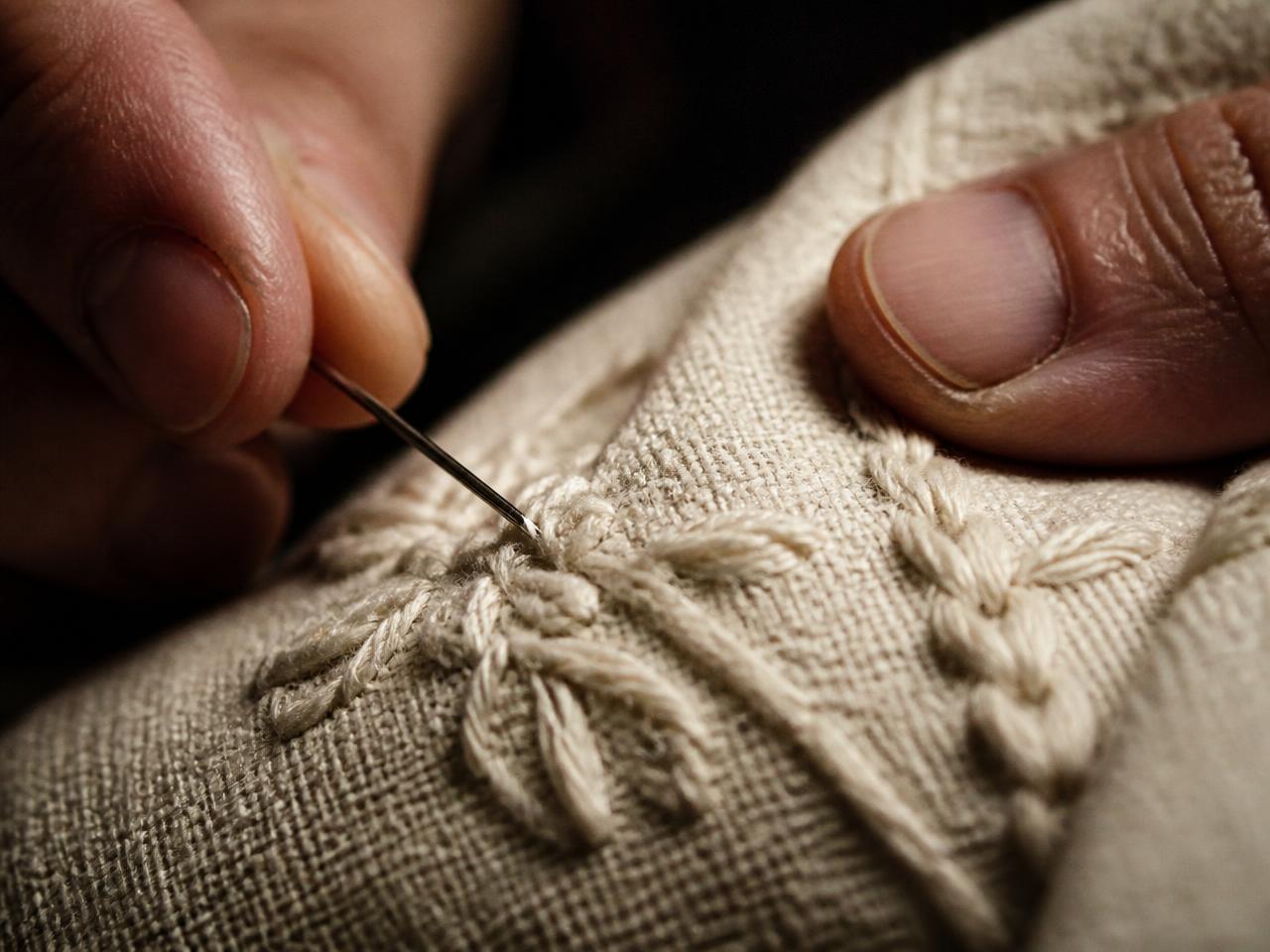 Hands embroidering cream thread into cotton